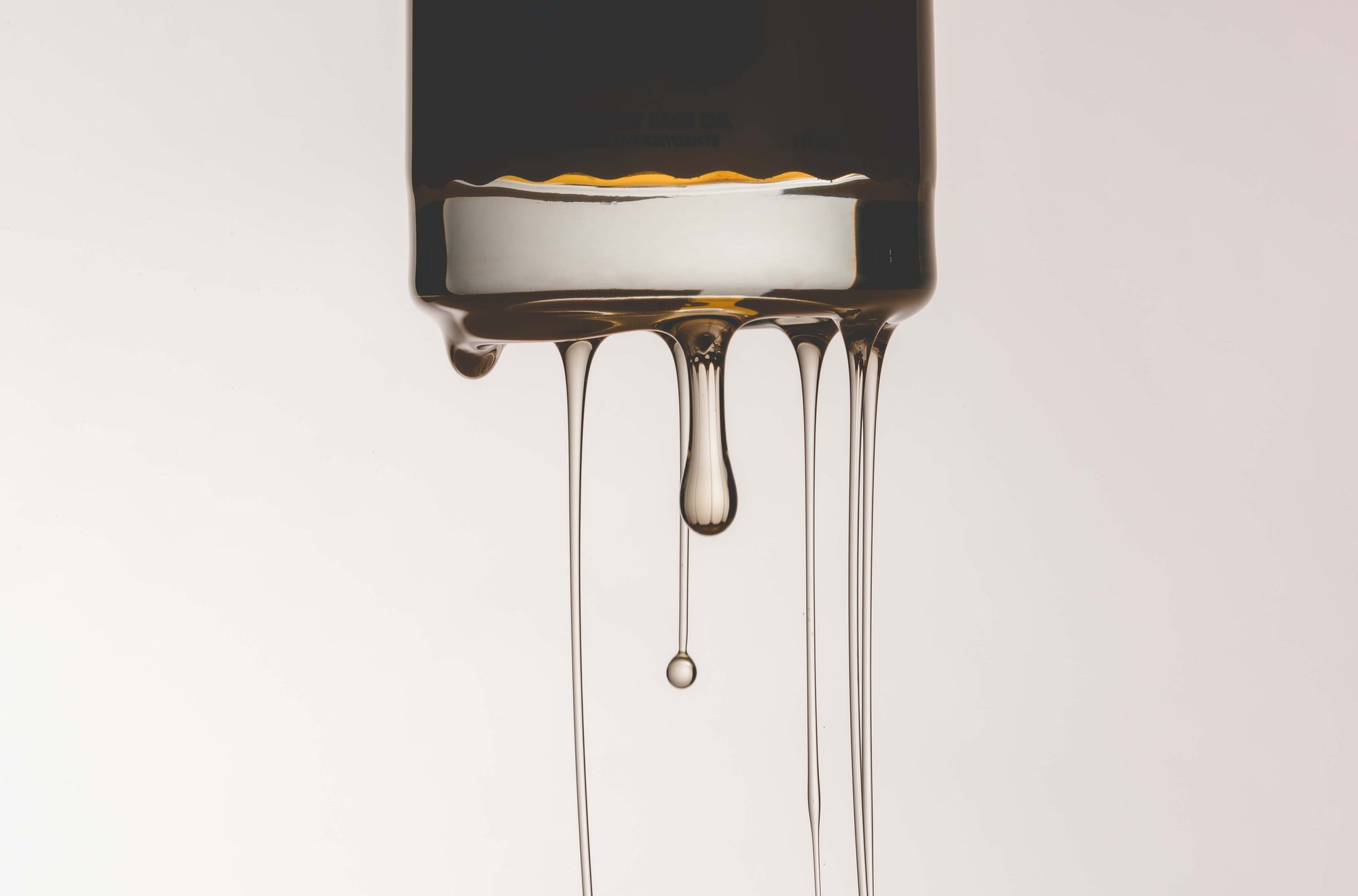 Close-up of Kid Sister’s Super Ego face oil dripping in slow, golden streams from the bottle, captured in a minimal, high-contrast shot that highlights the product’s luxurious texture.