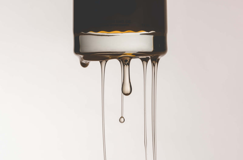 Close-up of Kid Sister’s Super Ego face oil dripping in slow, golden streams from the bottle, captured in a minimal, high-contrast shot that highlights the product’s luxurious texture.